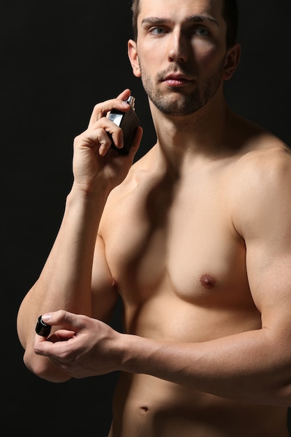 Handsome man using perfume on black surface