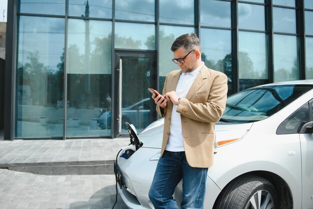 Handsome man using phone while car being charged