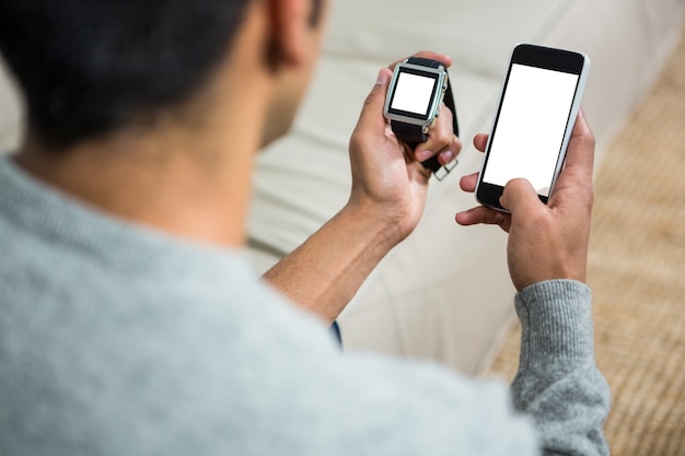 Photo handsome man using smartphone and smartwatch on the sofa