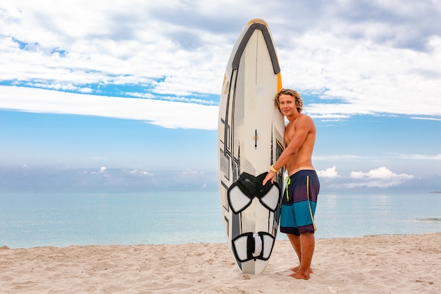 Camminata bella dell'uomo con la tavola da surf in bianco bianca aspetta l'onda per praticare il surf sul puntello dell'oceano del mare. concetto di sport, fitness, libertà, felicità, nuova vita moderna, vita bassa.