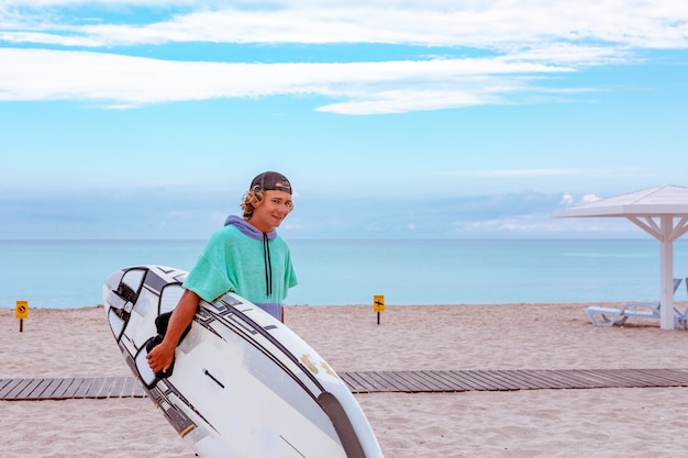 Handsome man walk with white blank surfing board wait for wave to surf spot at sea ocean shore. view from side. concept of sport, fitness, freedom, happiness, new modern life, hipster.