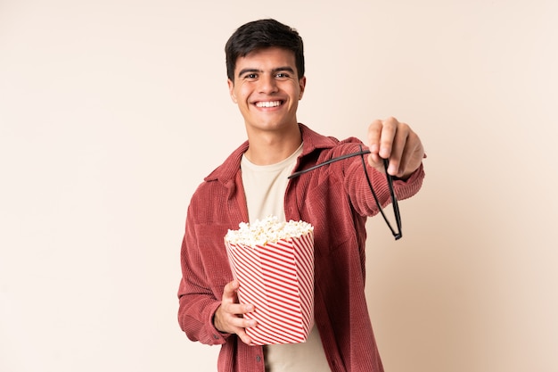 Handsome man over wall with 3d glasses and holding a big bucket of popcorns