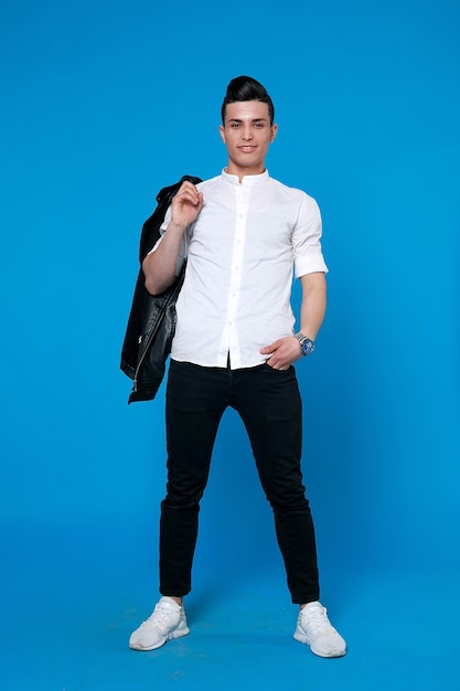 Handsome man wear black leather jacket. full length photo of a young casual man standing with his jacket on his shoulder and his hand in his pocket while looking into the camera. on blue background