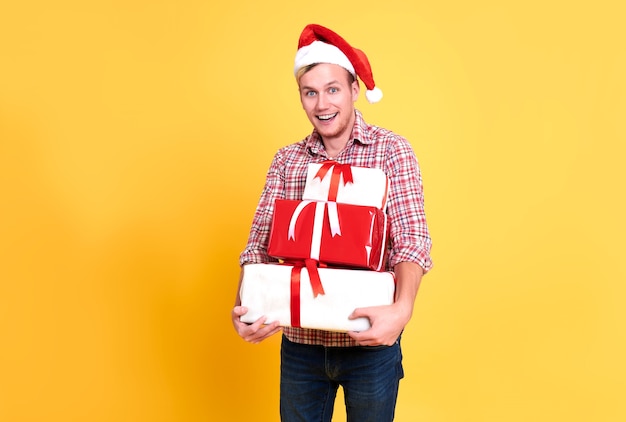 Handsome man wear santa hat holding a lot of gift box on yellow background.  christmas and happy new year concept.