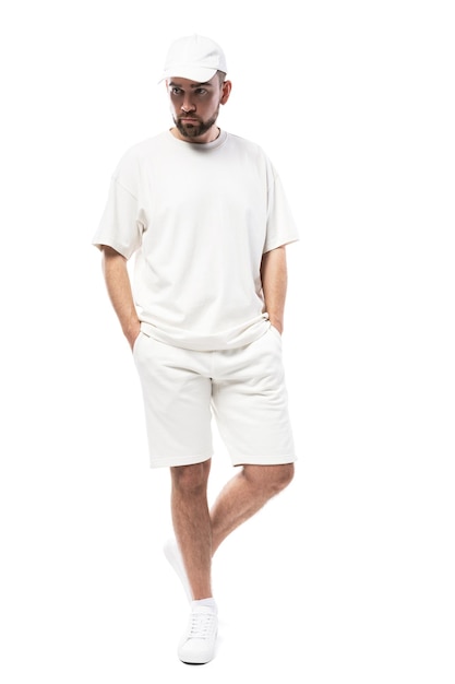 空白の白い帽子、Tシャツ、白い背景で隔離のショートパンツを着てハンサムな男