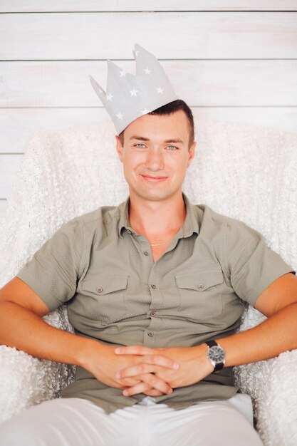 Handsome man wearing crown sitting in chair in studio