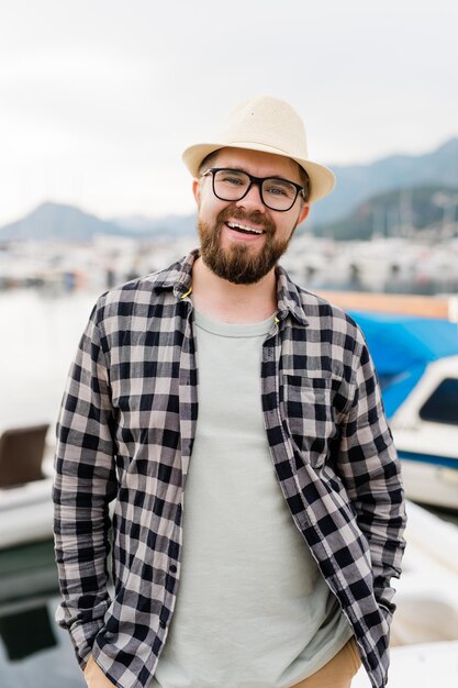 Handsome man wearing hat and glasses near marina with yachts portrait of laughing man with sea port