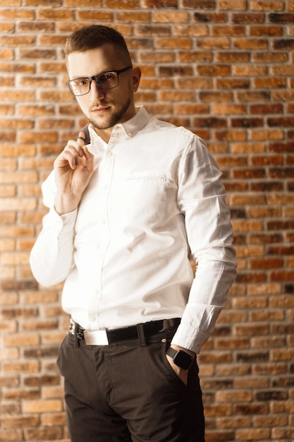 Handsome man in white shirt with glasses standing near red brick wall