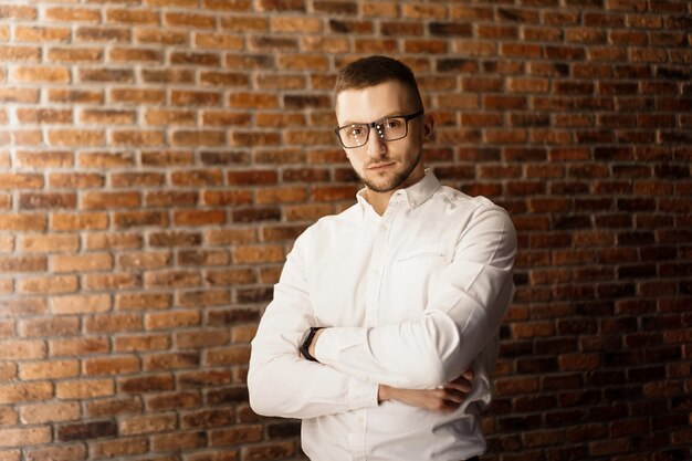 Handsome man in white shirt with glasses standing near red brick wall