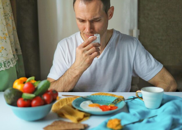 白いTシャツを着たハンサムな男が自宅で健康的な朝食とテーブルに座っています