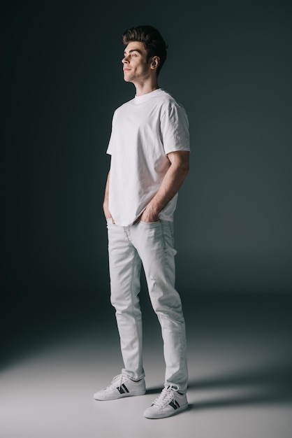 Handsome man in white tshirt and jeans with hands in pockets looking away