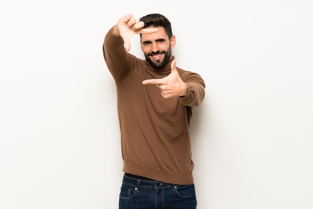 Handsome man over white wall focusing face. Framing symbol