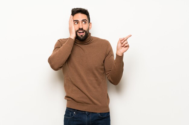 Handsome man over white wall pointing up and surprised