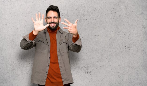 Handsome man with beard counting nine with fingers over textured wall