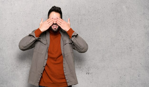 Handsome man with beard covering eyes by hands. 