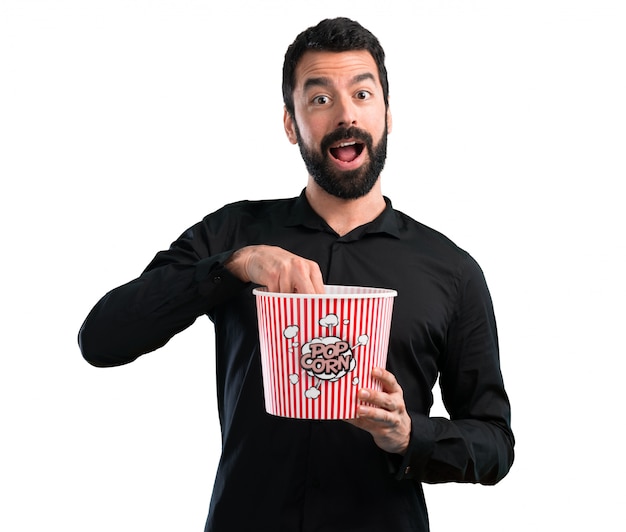 Uomo bello con la barba che mangia i popcorn su fondo bianco