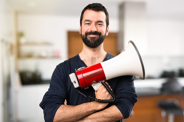 Uomo bello con la barba che tiene un megafono all'interno della casa