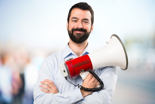 Handsome man with beard holding a megaphone on unfocused background