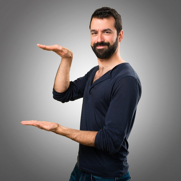 Handsome man with beard holding something on grey background