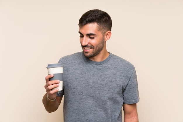 Handsome man with beard holding a take away coffee over isolated wall smiling a lot