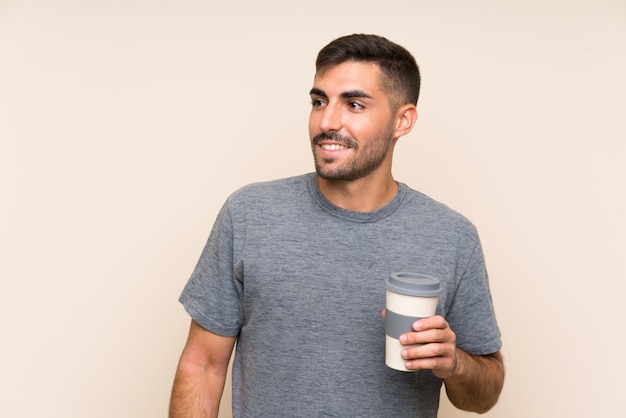 Handsome man with beard holding a take away coffee over isolated wall