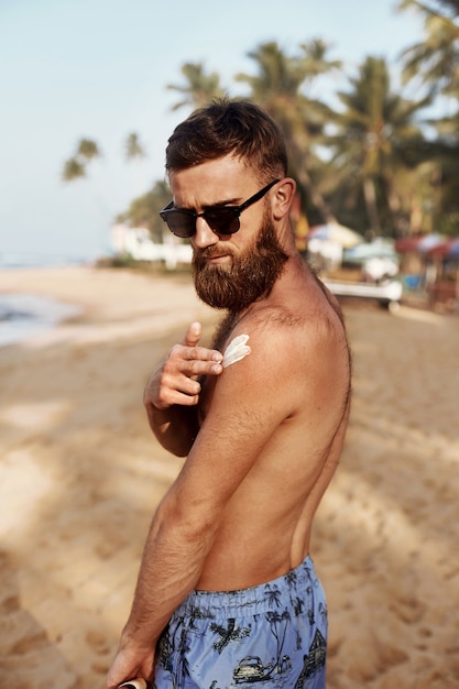 夏に日焼け止めローションボディで日光浴サングラスで、ひげを持つハンサムな男。