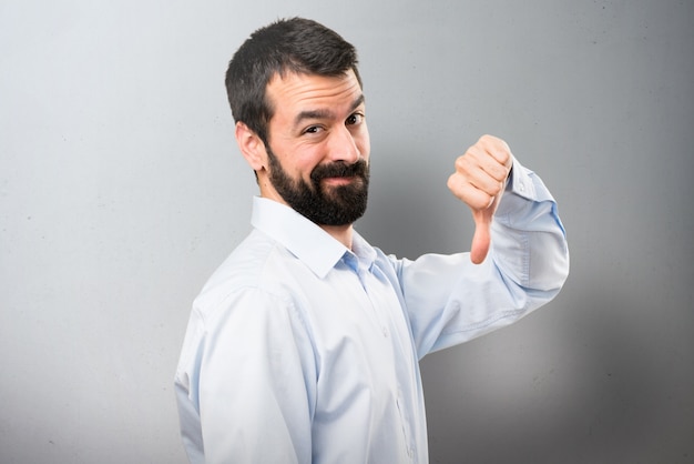 Handsome man with beard making bad signal on textured background