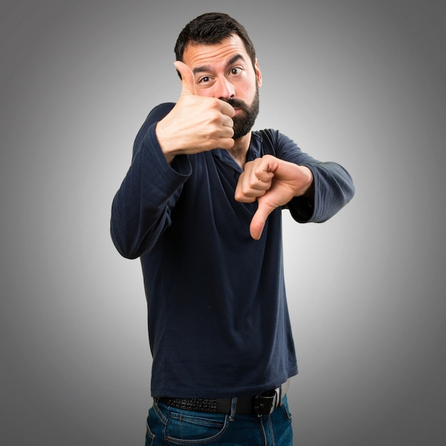 Handsome man with beard making good-bad sign on grey background