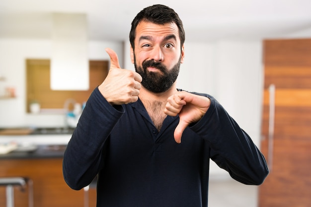 Handsome man with beard making good-bad sign inside house