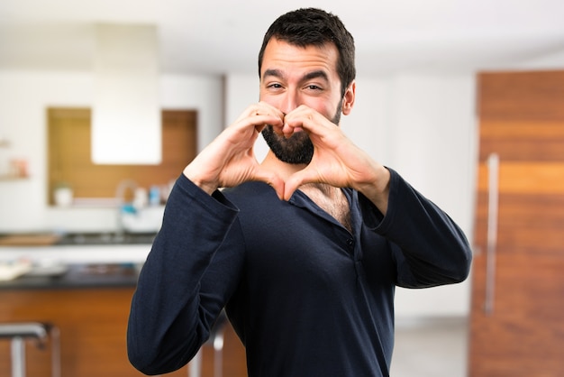 Uomo bello con la barba facendo un cuore con le mani all'interno della casa