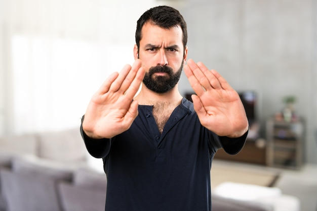 Handsome man with beard making stop sign inside house