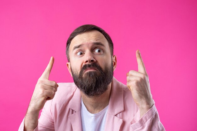 Handsome man with a beard in a pink jacket is thinking over an isolated red background