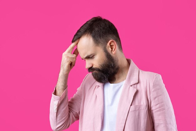 Handsome man with a beard in a pink jacket is thinking over an isolated red background