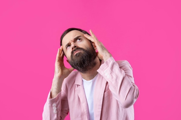 Handsome man with a beard in a pink jacket is thinking over an isolated red background