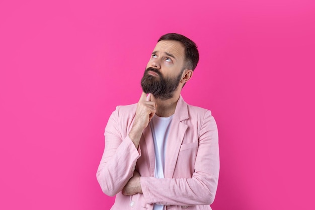 Красивый мужчина с бородой в розовой куртке думает на изолированном красном фоне