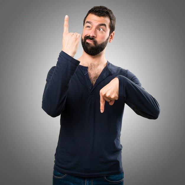 Handsome man with beard pointing to the laterals having doubts on grey background