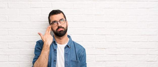 Handsome man with beard over white brick wall with problems making suicide gesture