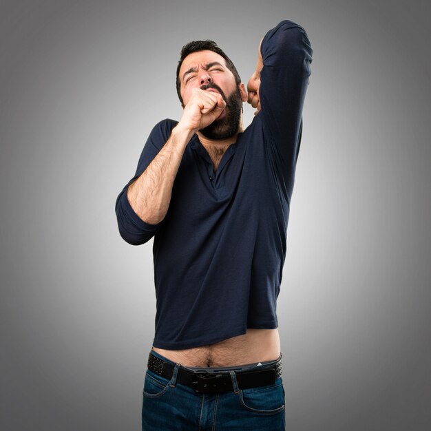 Handsome man with beard yawning on grey background