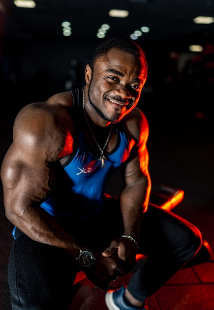 체육관에서 카메라에 포즈를 취하는 큰 근육을 가진 잘생긴 남자 어두운 밝은 배경 웃는 보디의 근접 촬영