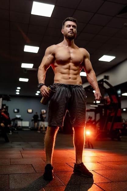 Handsome man with big muscles posing at the camera in the gym View from below Dark light background