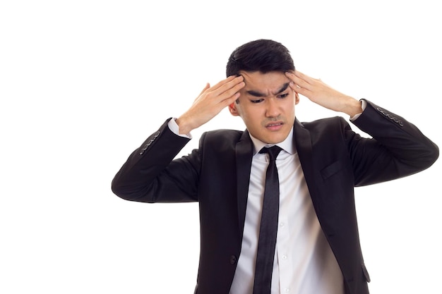 Handsome man with black hair in white shirt and black tuxedo with black tie holding his head