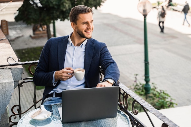 Handsome man with cup of coffee is working online using laptop in cafe. Remote work.