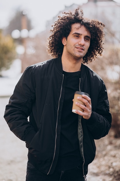 Handsome man with curly hair drinking coffee in the street