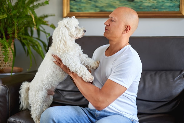 Handsome man with cute white dog at home on sofa