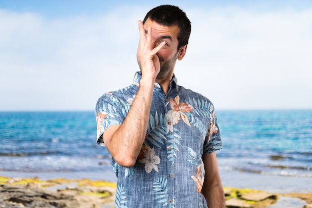 Uomo bello con la camicia di fiori facendo uno scherzo in spiaggia