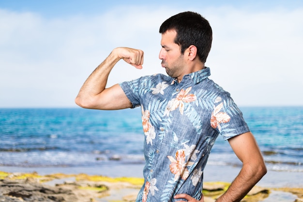 Uomo bello con camicia di fiori che fanno un gesto forte alla spiaggia