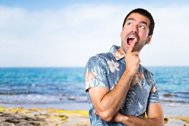 Handsome man with flower shirt making surprise gesture at the beach