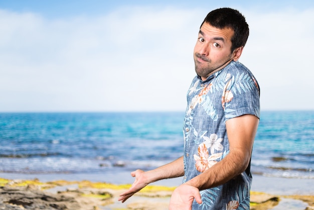 Handsome man with flower shirt making unimportant gesture at the beach