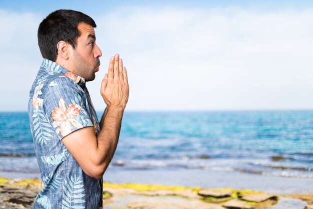 Handsome man with flower shirt pleading at the beach