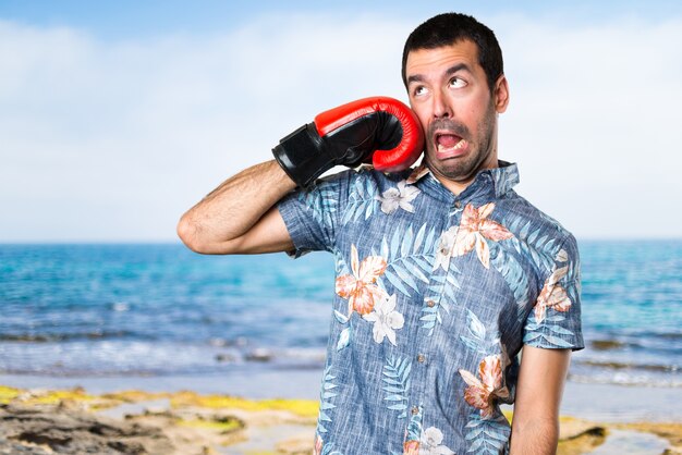 Handsome man with flower shirt with boxing gloves at the beach